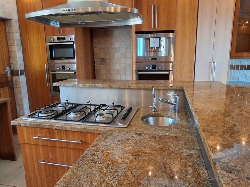 A spacious kitchen featuring granite countertops, wooden cabinetry, a gas hob, built-in oven, and integrated microwave, offering a functional and well-equipped cooking space.