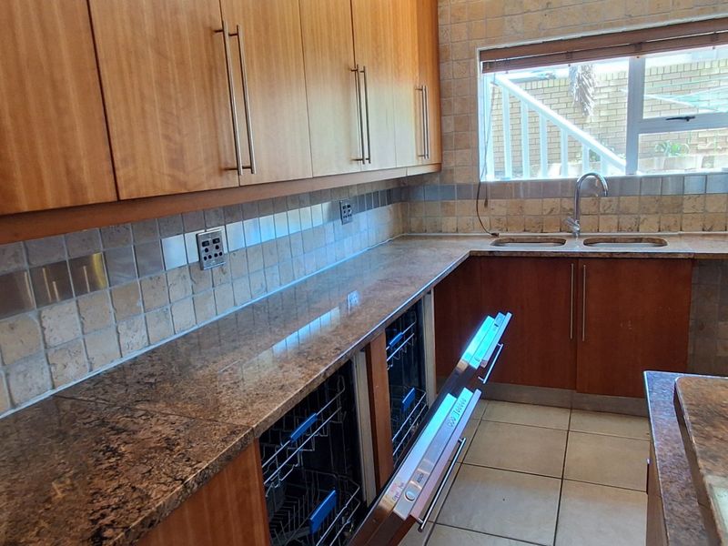 A functional kitchen featuring granite countertops, wooden cabinetry, a double basin sink, and tiled backsplash with integrated dishwasher space.
