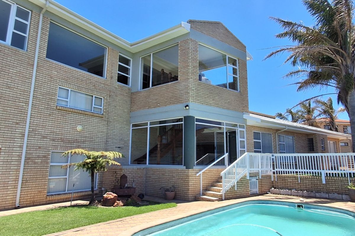 Rear view of a multi-story brick house featuring a swimming pool, paved deck, and large windows overlooking the garden area.