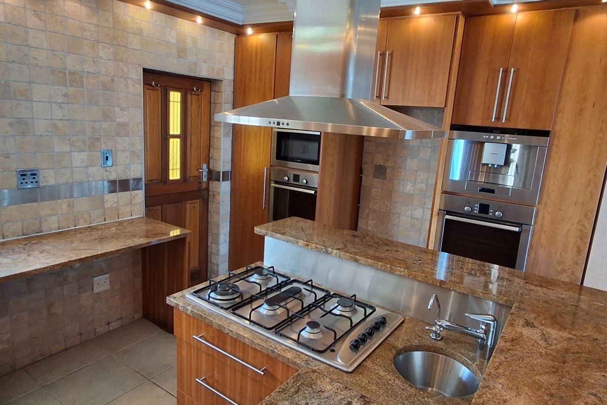 A well-equipped kitchen featuring granite countertops, built-in gas hob, stainless steel extractor, and integrated appliances with ample wooden cabinetry.