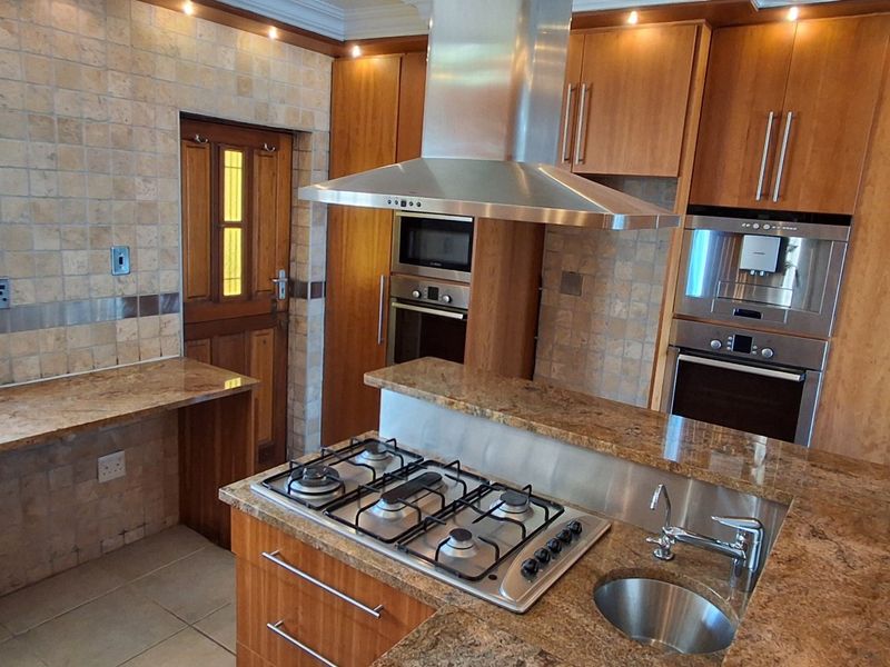 A well-equipped kitchen featuring granite countertops, built-in gas hob, stainless steel extractor, and integrated appliances with ample wooden cabinetry.