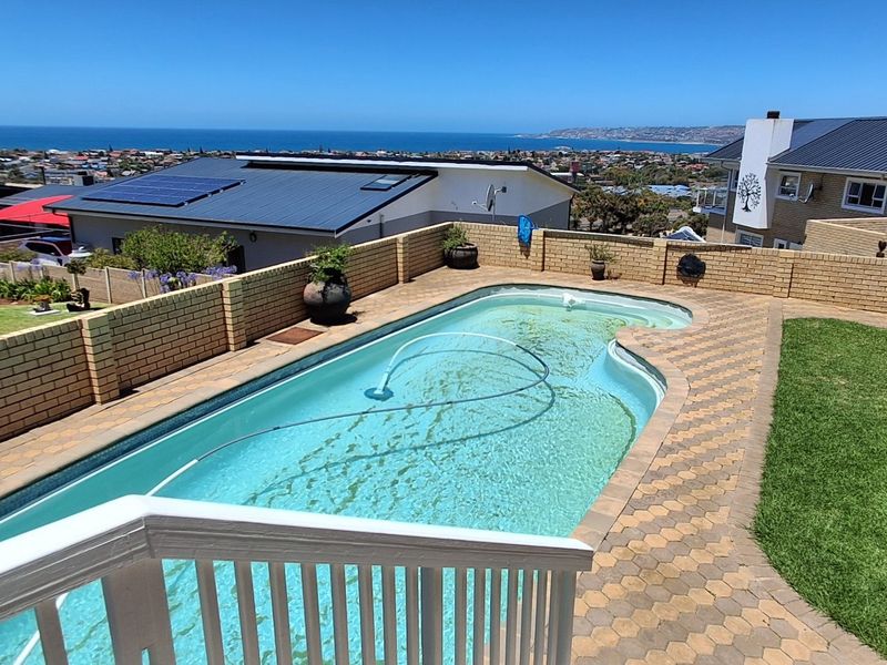 Outdoor pool area featuring a paved surround, brick boundary walls, and a lawn, offering elevated coastal and neighbourhood views.