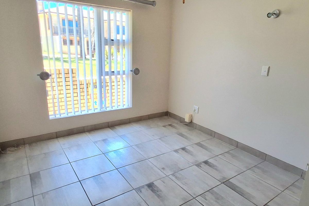 A bright, empty bedroom featuring neutral tiled flooring and vertical window blinds, providing a clean and versatile space ready for furnishing.