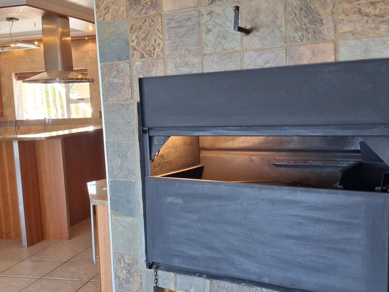 Open plan living area featuring a prominent stone-clad built-in fireplace and a functional kitchen with wooden cabinetry and granite countertops.
