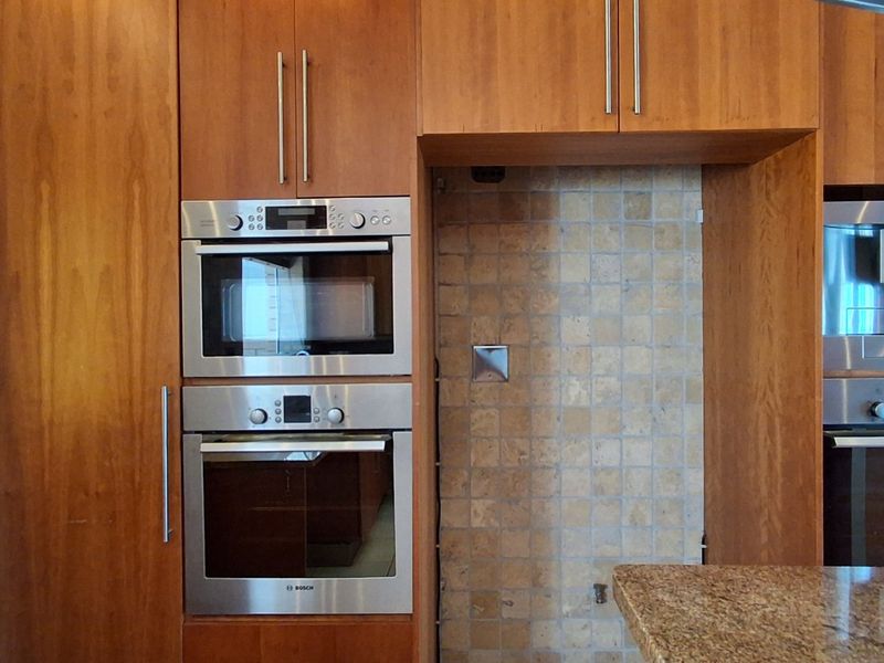 Kitchen wall featuring integrated stainless steel appliances, including an oven, microwave, and coffee machine, set within timber cabinetry and stone countertops.