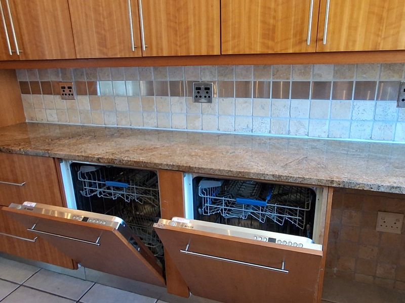 Kitchen area featuring granite countertops, tiled backsplash, and dual integrated dishwashers with wooden cabinetry.