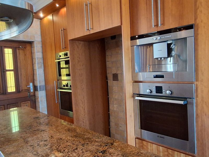 A well-equipped kitchen featuring warm wooden cabinetry, granite countertops, and integrated stainless steel appliances including an oven and coffee machine.