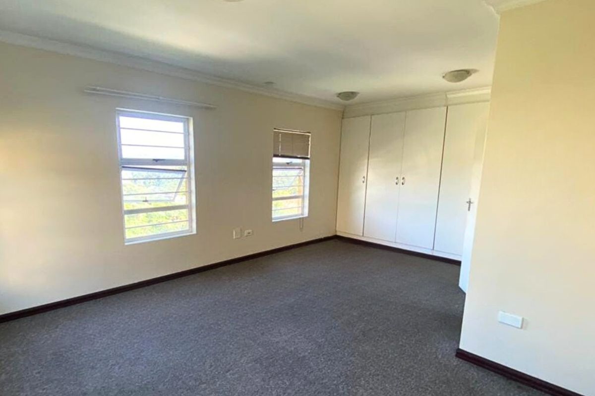 Spacious bedroom featuring neutral walls, carpeted flooring, and ample built-in cupboard storage with natural light from louvered windows.