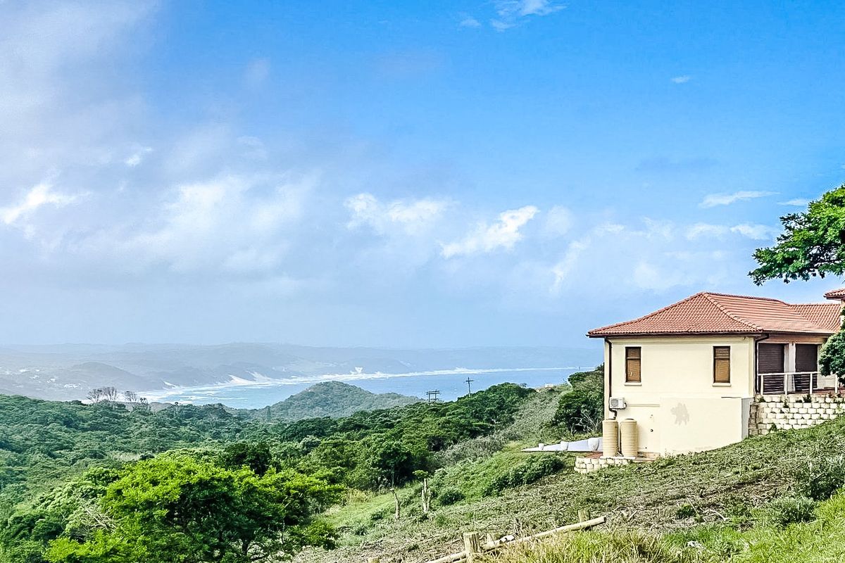 A scenic elevated view overlooking lush coastal landscape and the ocean, featuring a residential structure with water storage tanks and a tiled roof.