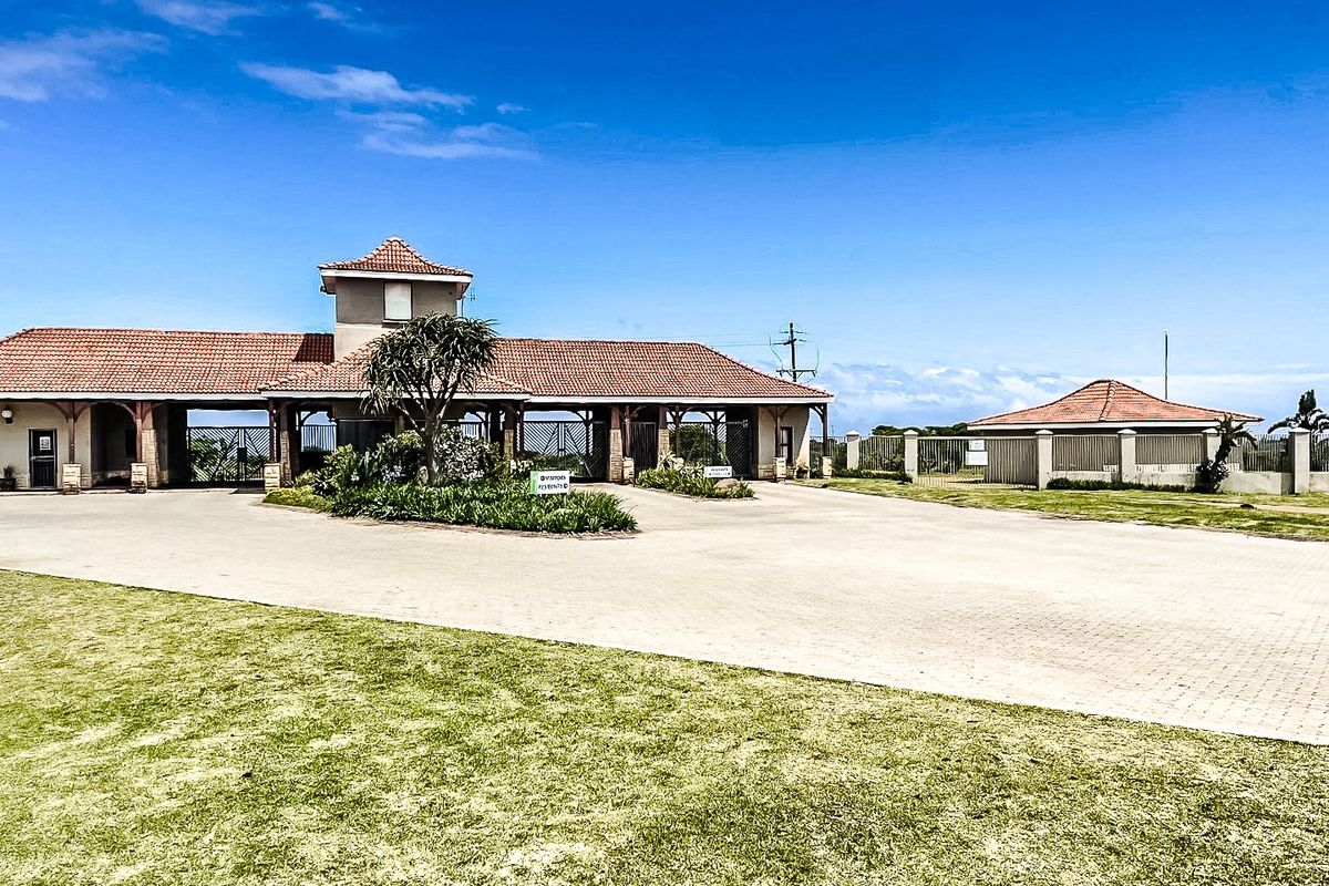 A well-maintained gated residential estate entrance featuring a paved driveway, security access point, and tiled roof structures.