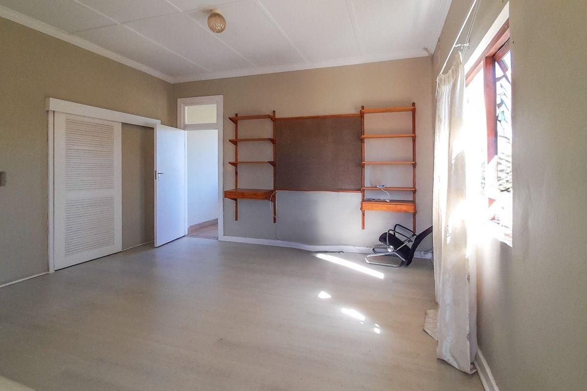 A spacious, empty bedroom featuring built-in wall shelving, a sliding door, and a coved ceiling, offering a blank canvas for renovation.