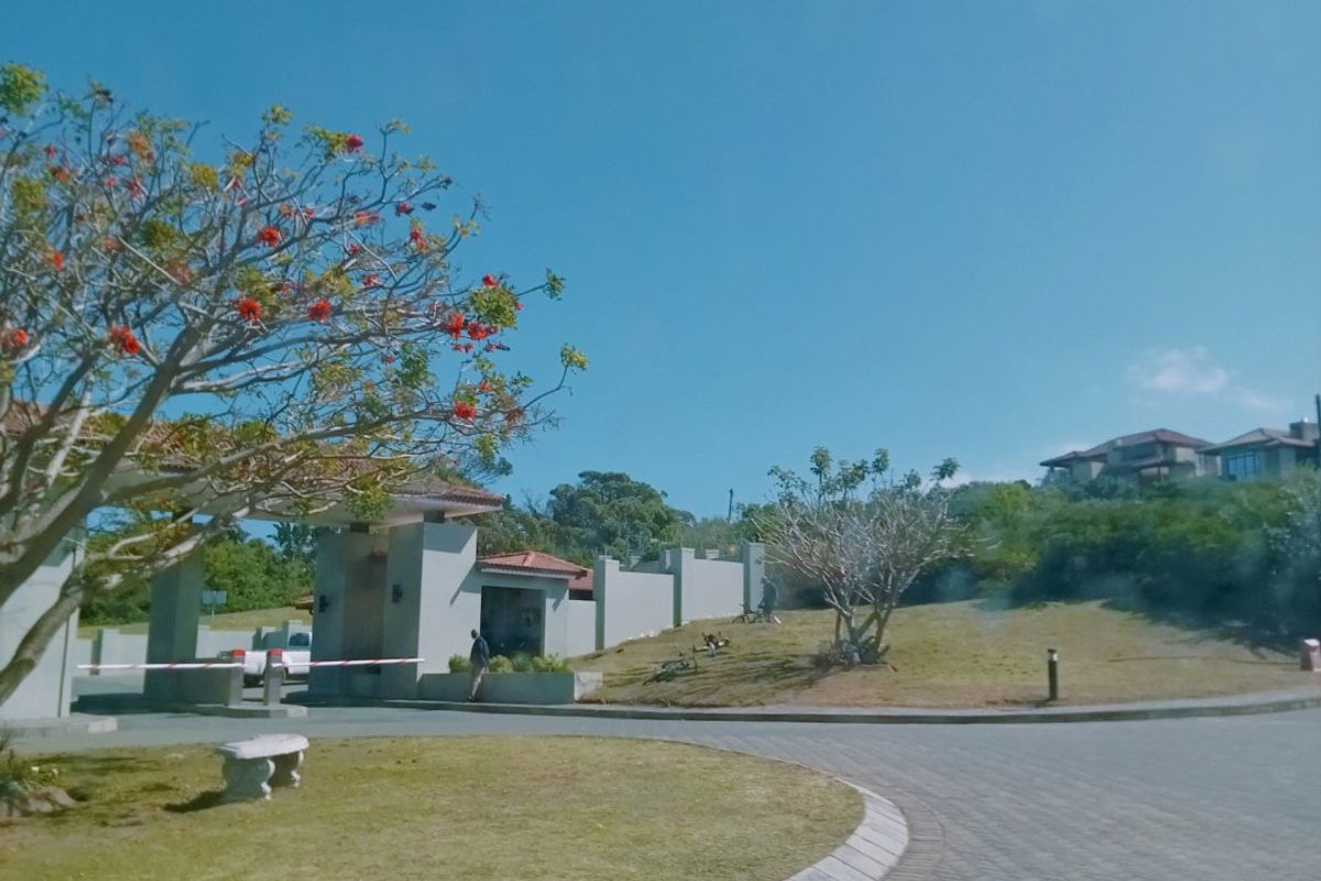 View of the residential estate entrance featuring a paved driveway, security gatehouse, and well-maintained landscaped grounds.