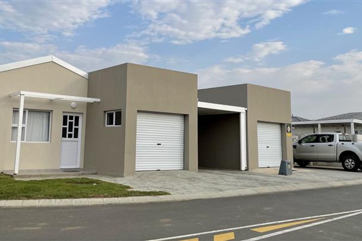 Modern single-story residential facade featuring a paved driveway, two roller garage doors, and an integrated carport.