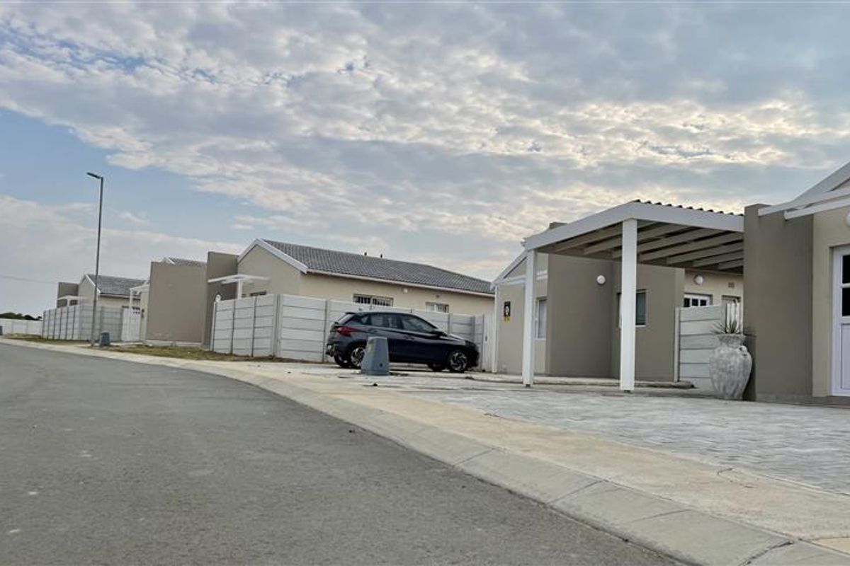Street view of a modern residential development featuring paved driveways, covered carports, and precast boundary walls.