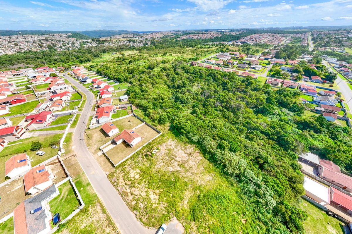 Aerial view of a vacant residential plot situated within an established suburban neighborhood, featuring surrounding homes and natural vegetation.