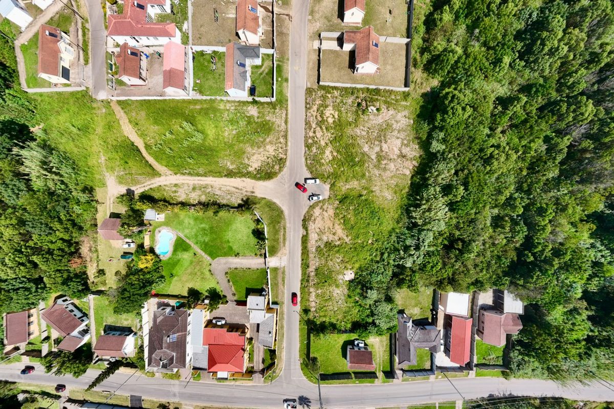 An aerial view of a residential neighborhood showing vacant land plots, existing houses, and surrounding greenery.