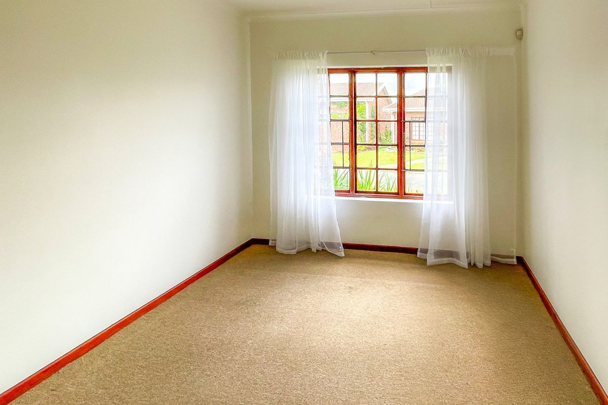 A bright, empty bedroom featuring neutral carpeting, wooden window frames, and clean white walls, offering a blank canvas for personalization.