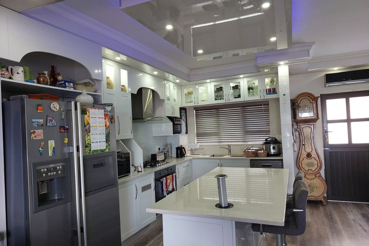 Modern kitchen featuring white cabinetry, stone countertops, a central island, integrated extractor fan, and a drop ceiling with recessed lighting.