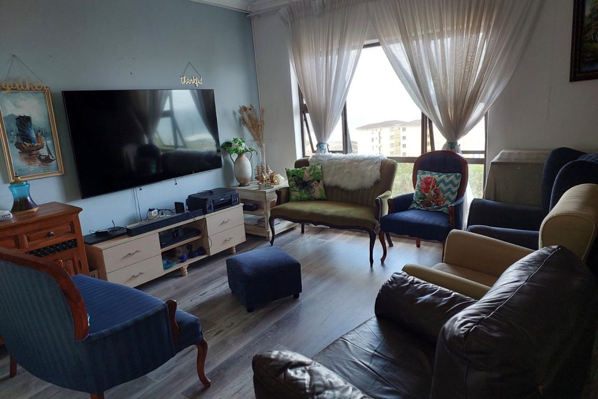 A comfortable living room featuring wood-look laminate flooring, large windows with natural light, and a neutral wall finish.