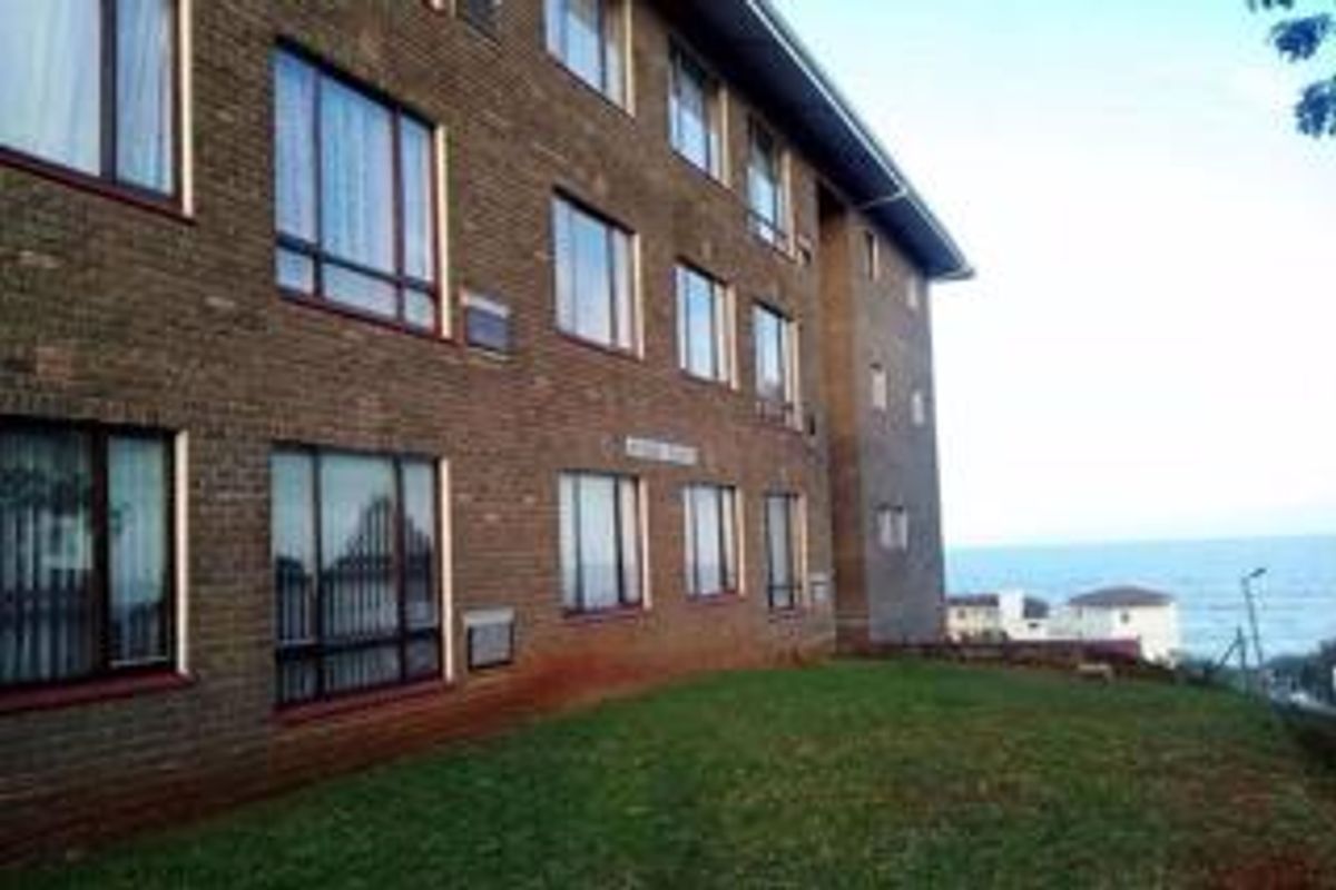 Exterior view of a multi-story brick apartment building featuring large windows and a grassy lawn area with coastal views.