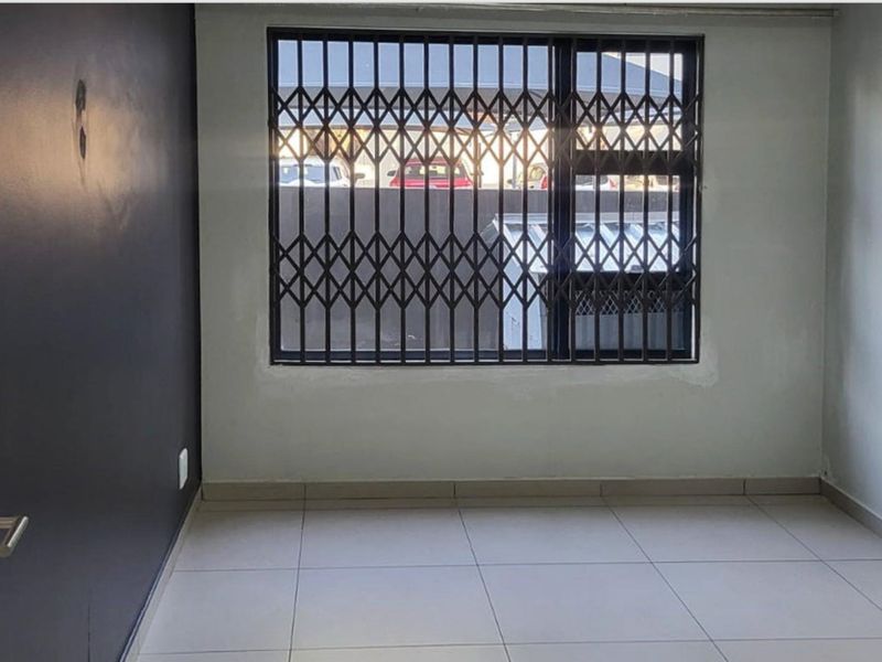 An empty bedroom featuring tiled flooring and a security gate on the window, requiring minor cosmetic repairs to the walls and paintwork.