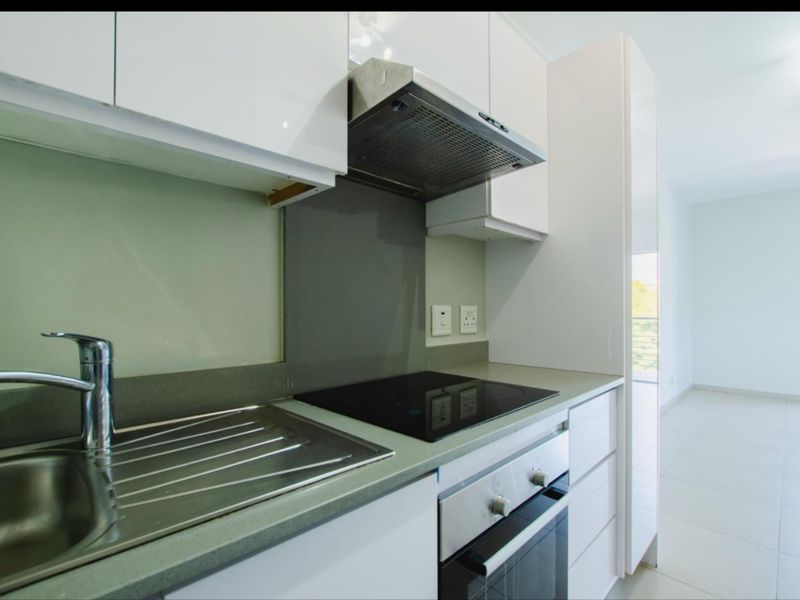 Modern kitchen featuring sleek white cabinetry, stone countertops, built-in oven, electric hob, and stainless steel sink, offering a clean and functional workspace.