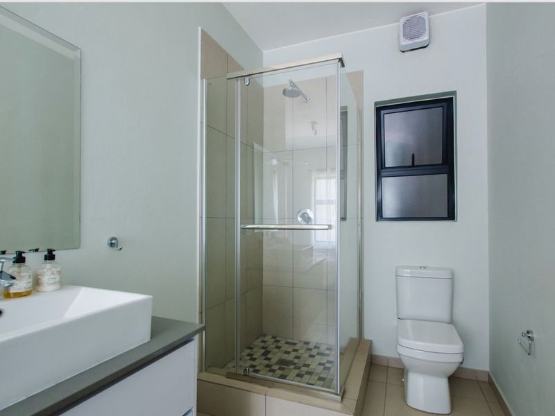 A clean, modern bathroom featuring a glass-enclosed shower, a contemporary vanity basin with storage, and a standard toilet.