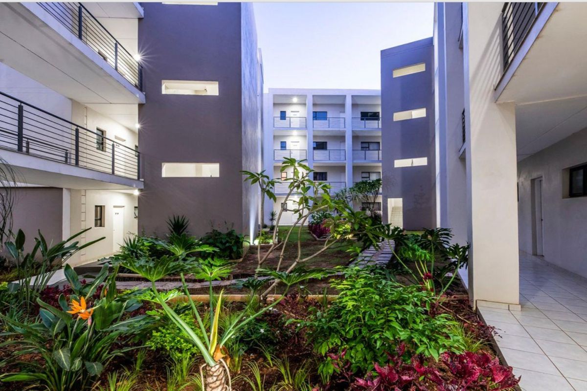 A well-maintained apartment complex courtyard featuring landscaped gardens, paved pathways, and modern multi-story residential blocks with private balconies.