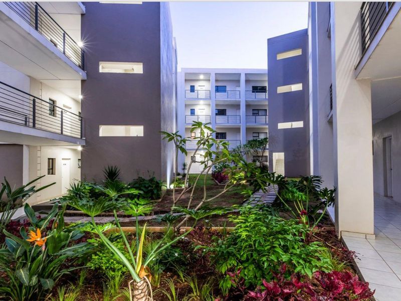 A well-maintained apartment complex courtyard featuring landscaped gardens, paved pathways, and modern multi-story residential blocks with private balconies.