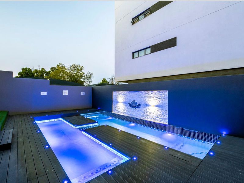 Modern apartment complex pool area featuring a sleek swimming pool, timber decking, and an illuminated feature wall with a water fountain.