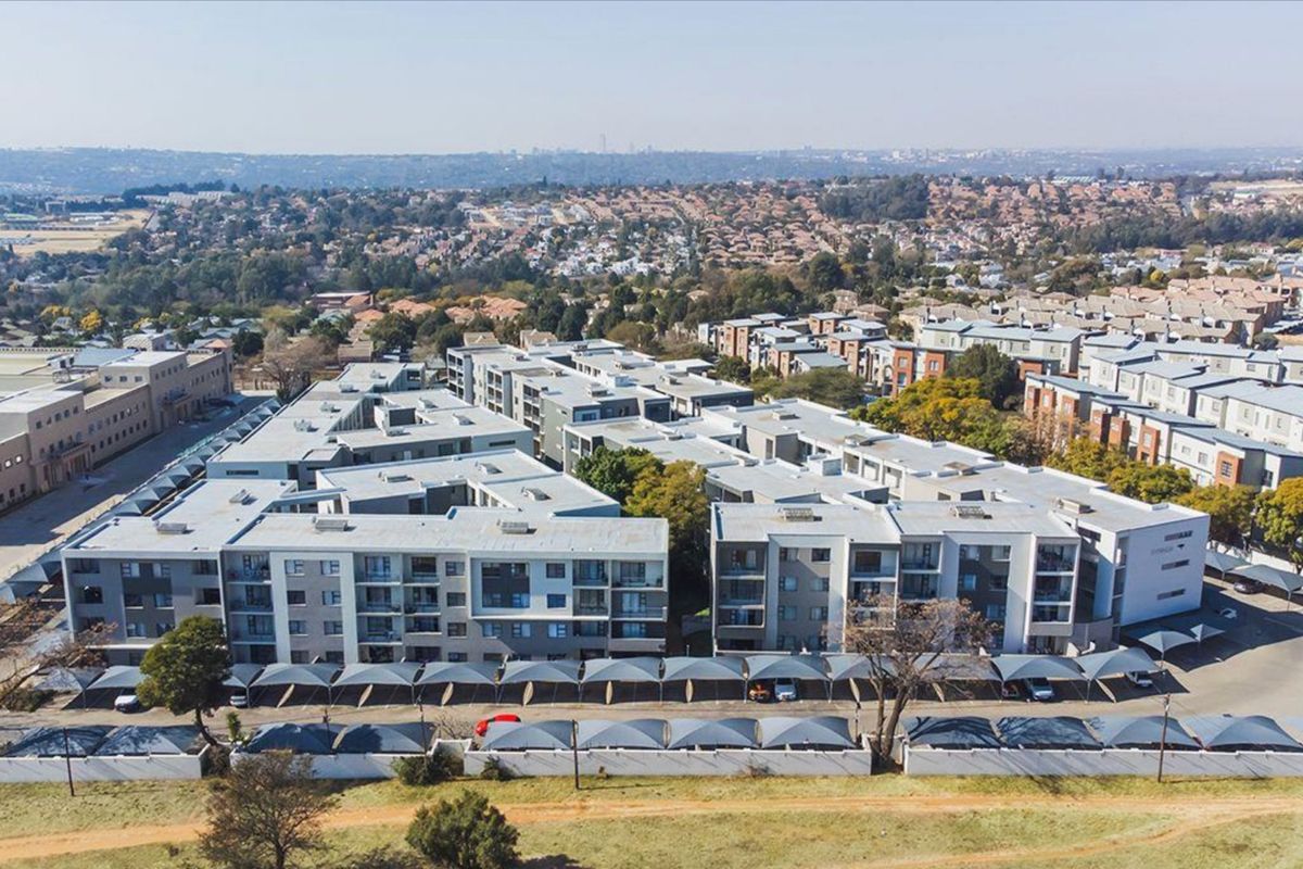 Aerial view of a modern multi-story apartment complex featuring extensive shaded parking facilities and surrounding residential neighborhood.