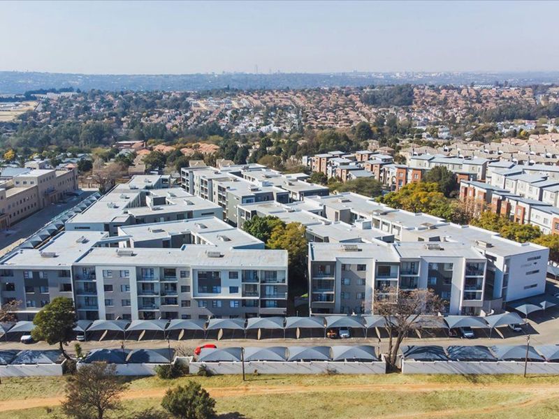 Aerial view of a modern multi-story apartment complex featuring extensive shaded parking facilities and surrounding residential neighborhood.