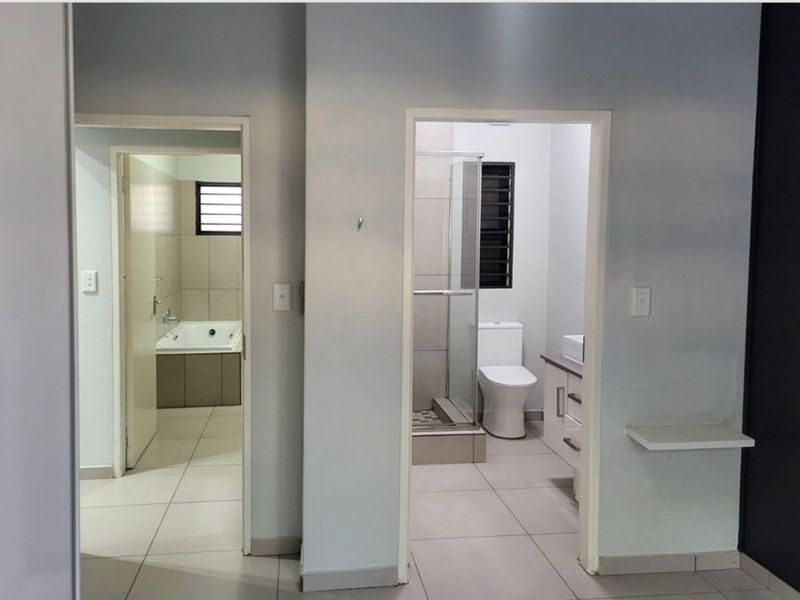 A view from a hallway looking into two separate bathroom areas, featuring tiled floors, a shower enclosure, a bathtub, and a modern vanity.