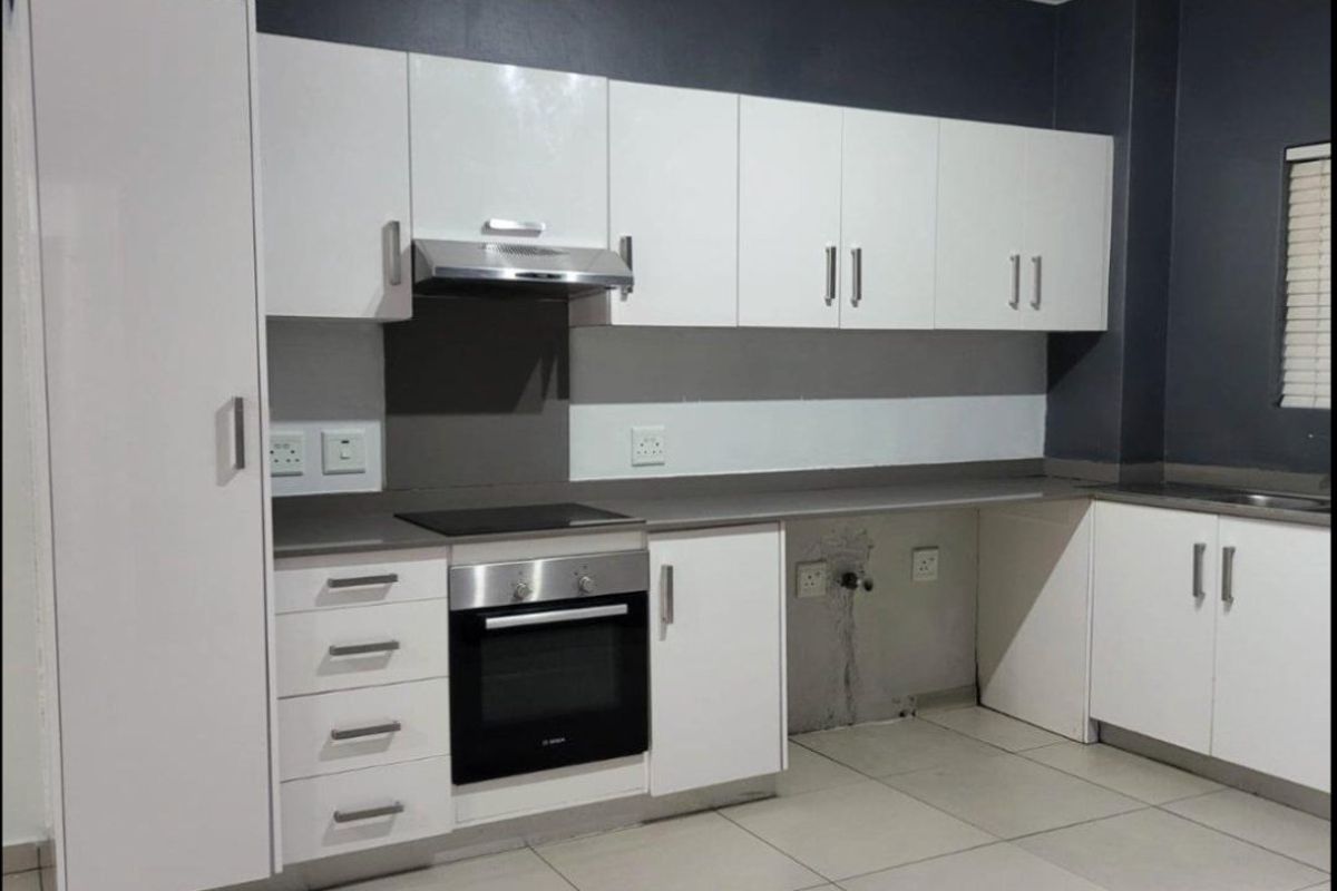 Modern kitchen featuring white cabinetry, built-in oven and hob, extractor fan, and tiled flooring. The space is currently vacant and ready for finishing touches.