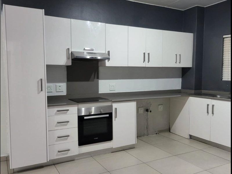 Modern kitchen featuring white cabinetry, built-in oven and hob, extractor fan, and tiled flooring. The space is currently vacant and ready for finishing touches.