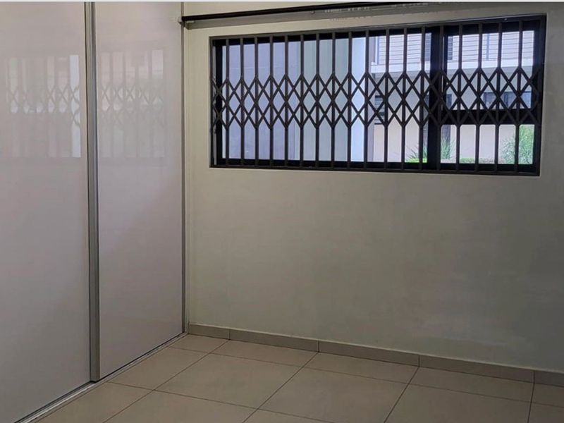 A clean, empty bedroom featuring tiled flooring, a built-in sliding door wardrobe, and a window fitted with a security gate.