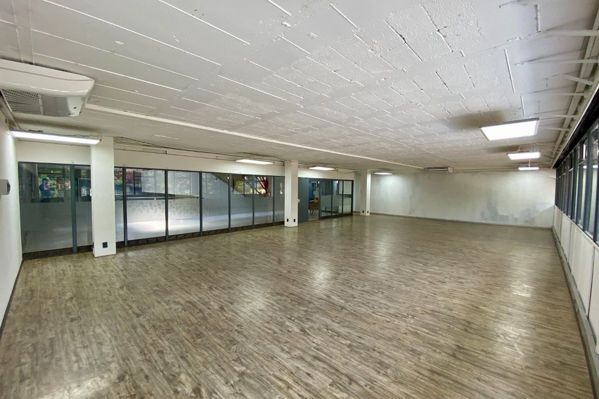 Spacious open-plan commercial office area featuring wood-look flooring, exposed concrete ceilings, and extensive glass partitioning for natural light.