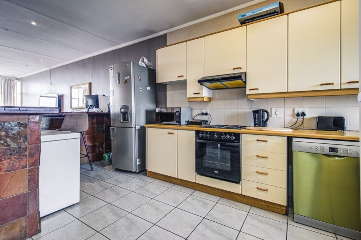 A functional kitchen featuring built-in cabinetry, a tiled backsplash, integrated oven and hob, and a stone-clad breakfast bar opening into the living area.