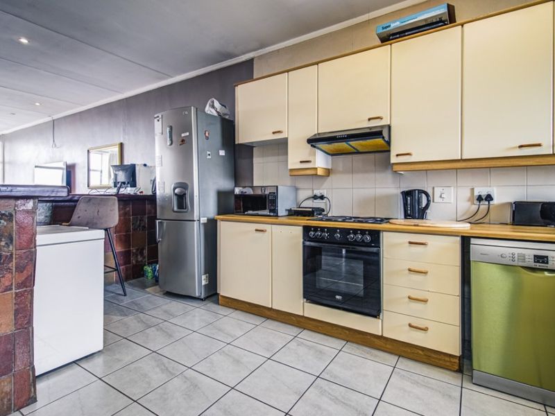 A functional kitchen featuring built-in cabinetry, a tiled backsplash, integrated oven and hob, and a stone-clad breakfast bar opening into the living area.