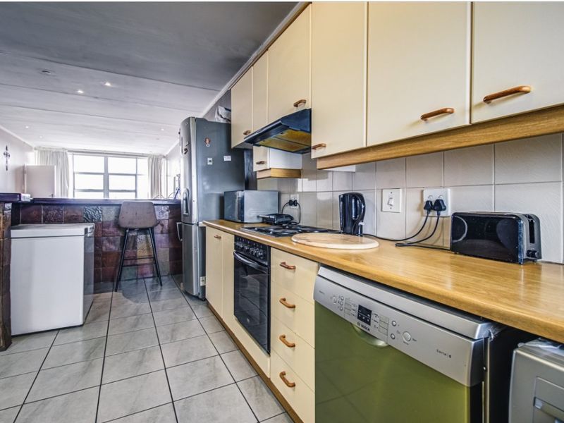 Functional kitchen featuring laminate countertops, tiled backsplash, built-in oven and hob, and a breakfast bar overlooking the living area.