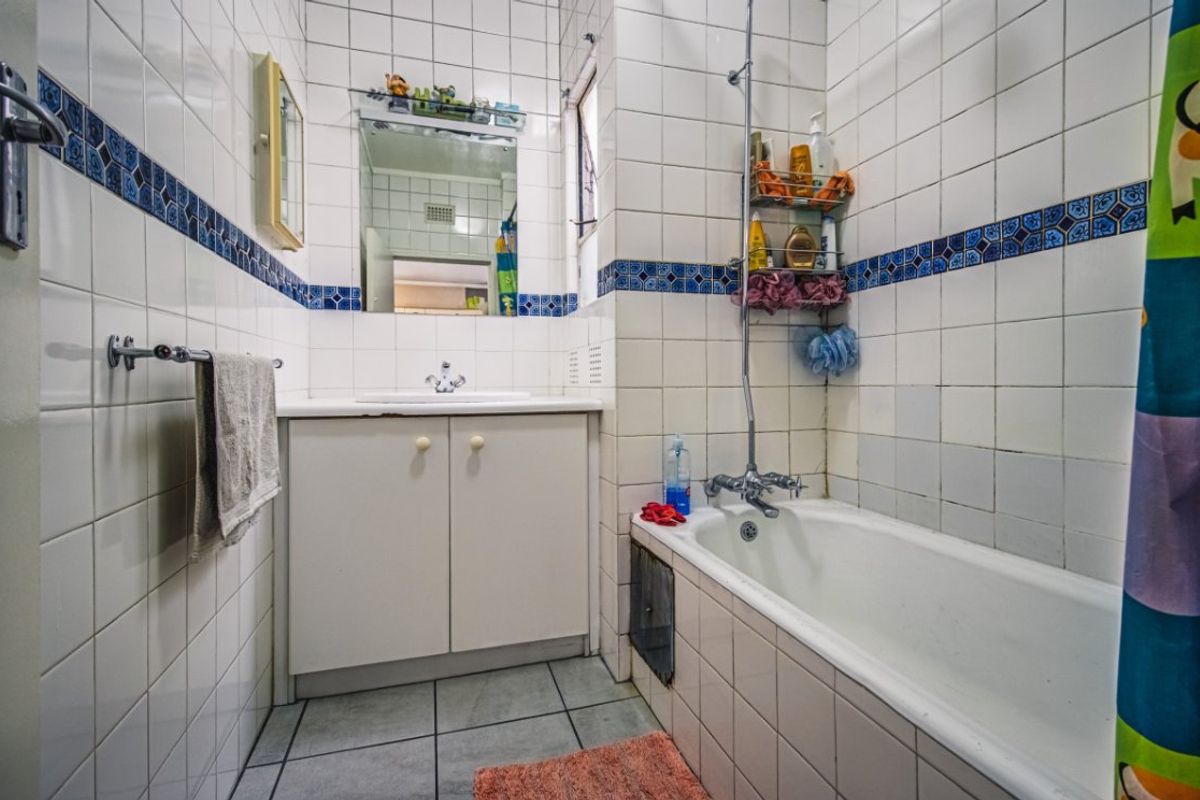 A dated bathroom featuring a built-in vanity, bathtub with shower mixer, and tiled finishes throughout, offering potential for modernization.