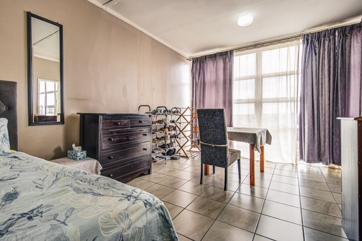 A bedroom featuring tiled flooring and a large window with curtains. The walls show signs of wear and staining, suggesting a need for refurbishment.