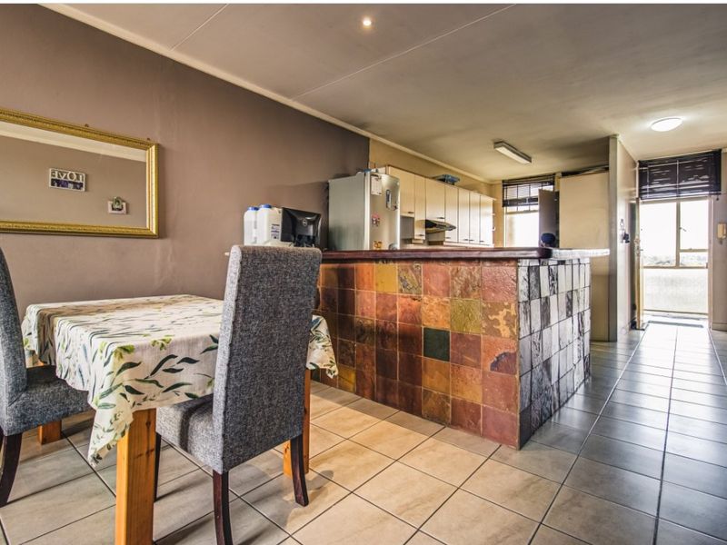 Open plan living and kitchen area featuring a tiled breakfast bar, ceramic flooring, and built-in cabinetry with direct access to an outdoor balcony.