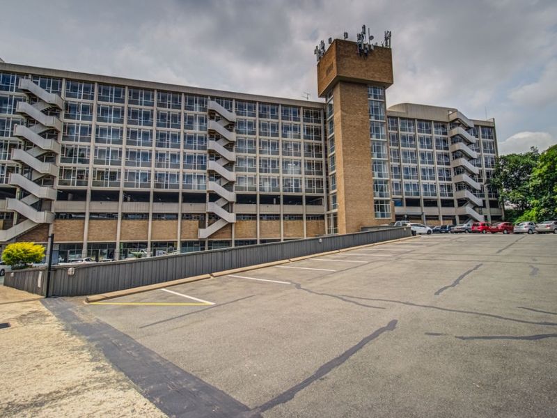 Exterior view of a large multi-story apartment building featuring a brick facade, external fire escape staircases, and an adjacent asphalt parking lot.