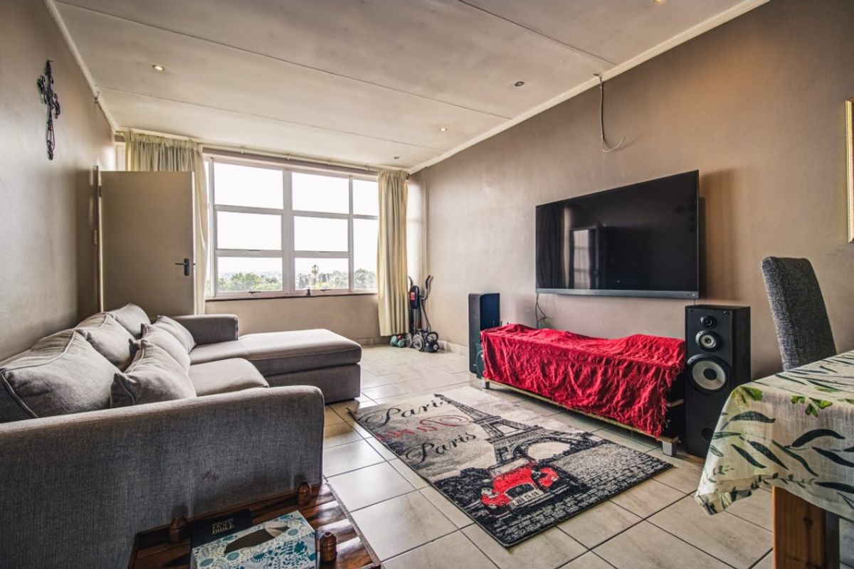 A spacious living room featuring tiled flooring, recessed downlighting, and a large window providing natural light and exterior views.
