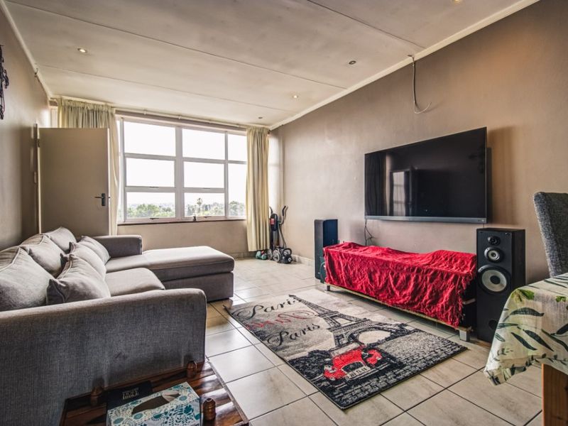 A spacious living room featuring tiled flooring, recessed downlighting, and a large window providing natural light and exterior views.