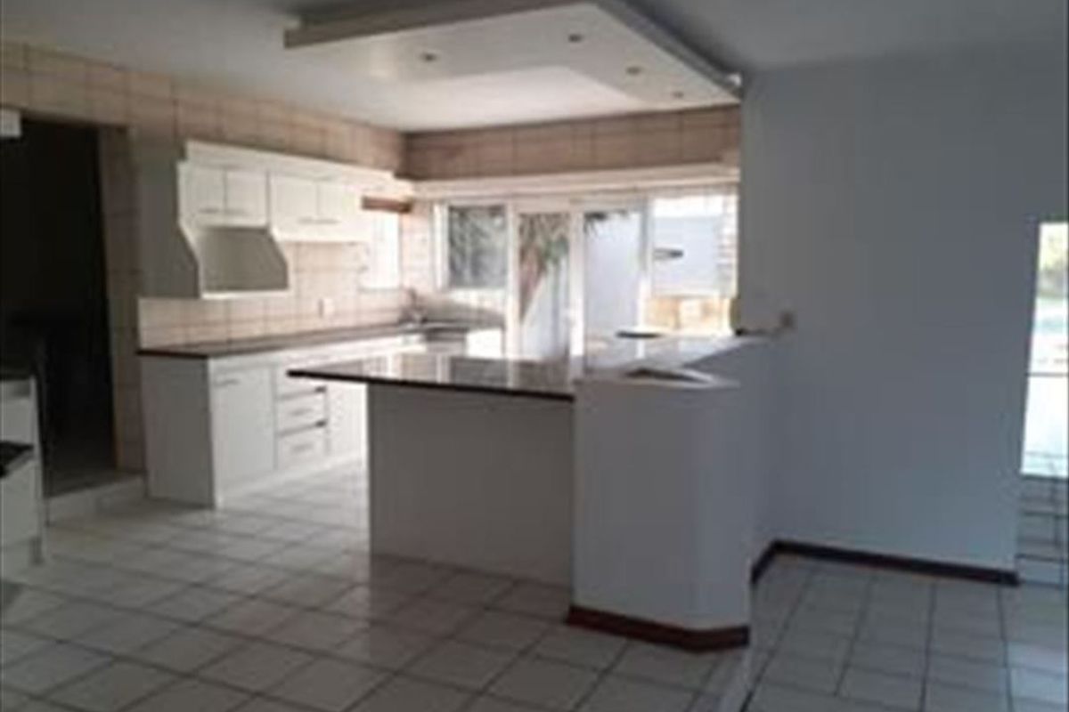A spacious, empty kitchen featuring white built-in cabinetry, granite countertops, a breakfast bar, and tiled flooring with recessed ceiling lighting.