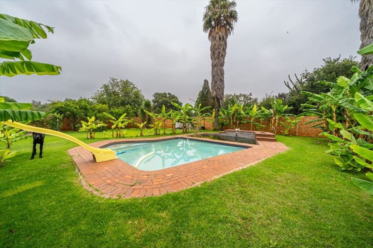 A private backyard featuring a swimming pool with brick coping, a slide, and a landscaped garden area enclosed by a brick boundary wall.