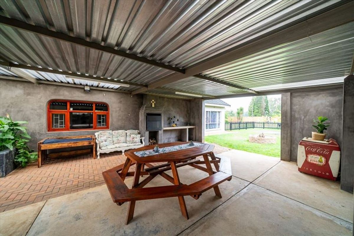 Covered outdoor patio area featuring a built-in braai, concrete prep counter, and a mix of brick and concrete flooring, overlooking the rear garden.