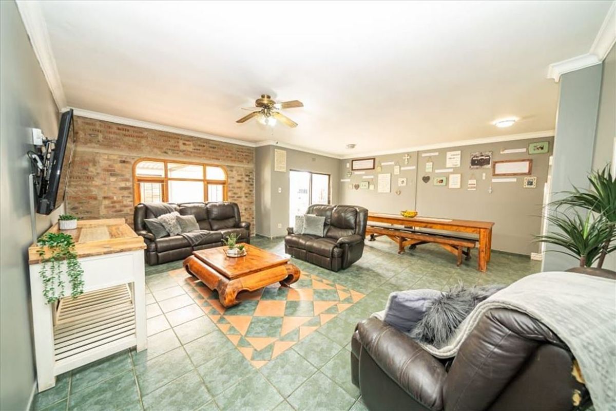 Spacious living area featuring exposed brick accent wall, tiled flooring, and ceiling fan, offering a comfortable and versatile layout for family relaxation.